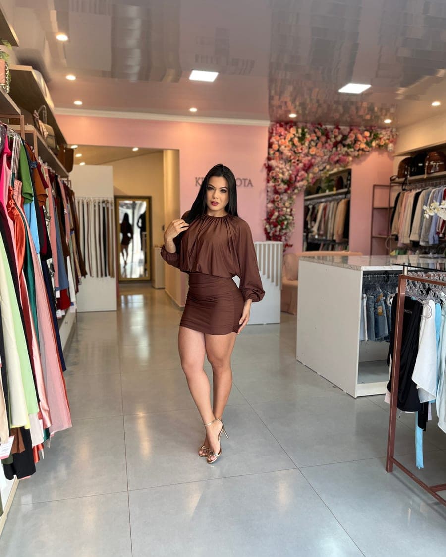 Sayuri Castro com blusa e saia marrom no corredor da loja